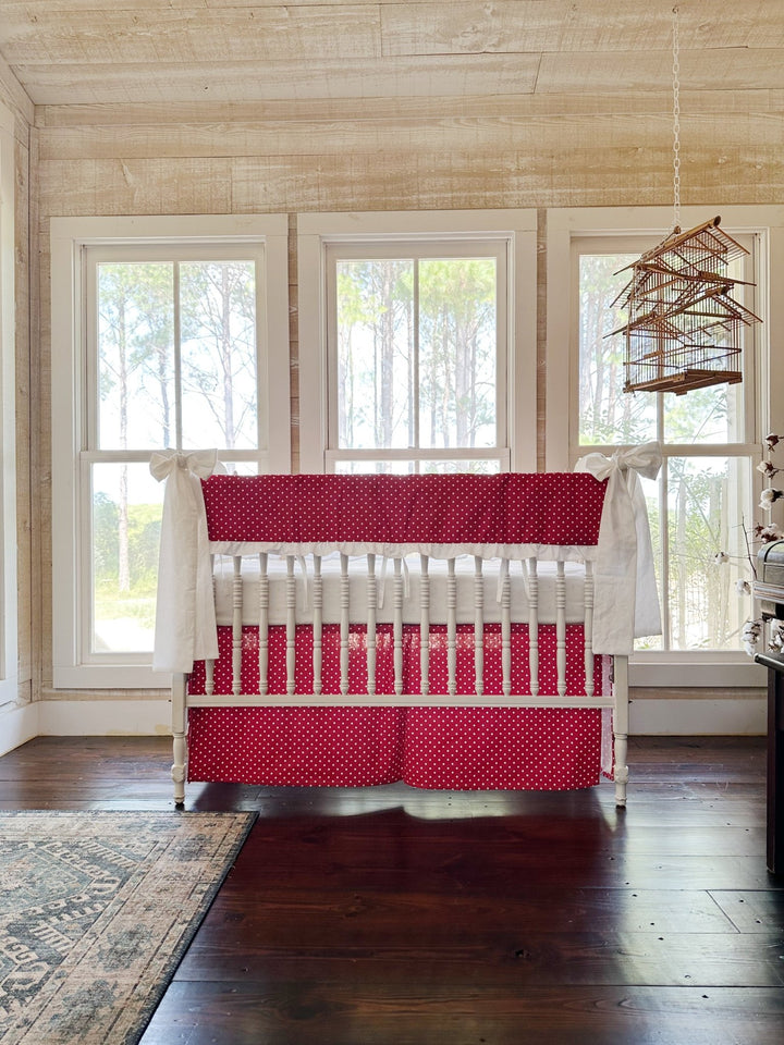 The red polka dot crib set in a pine-paneled nursery with three tall windows and a hanging birdcage