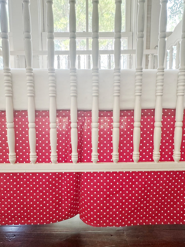 The skirt filling the frame through the crib spindles — small white dots and the inverted center pleat