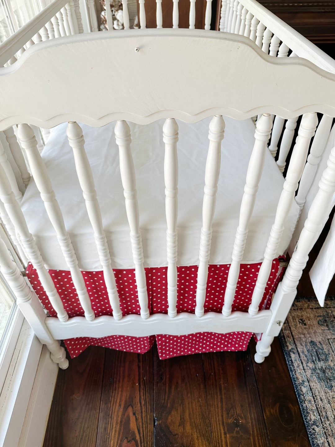 Seen from the end of the crib, the pleated dotted skirt beneath a plain white sheet