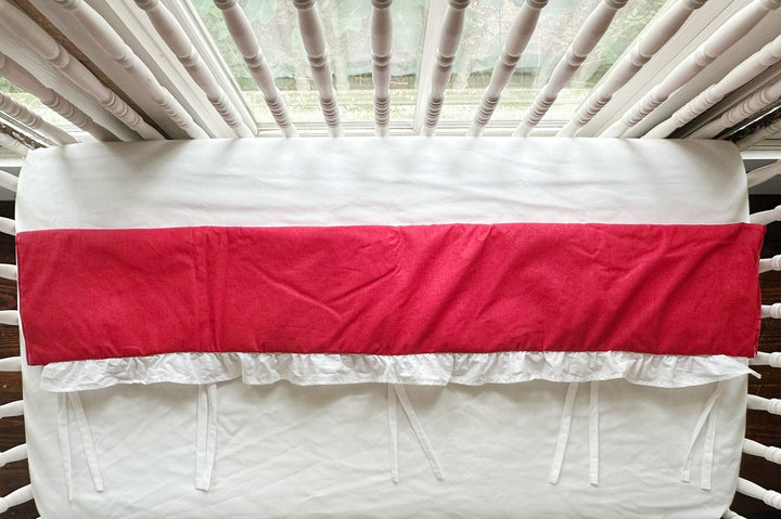 Overhead view of the red rail cover folded over, white ruffle and ties hanging below the solid red panel