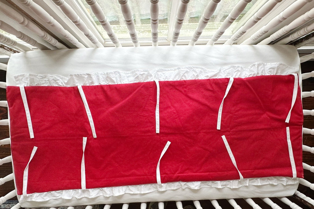 Cherry red ruffled crib rail cover laid flat, white ruffle along the edge and every white tie spread out