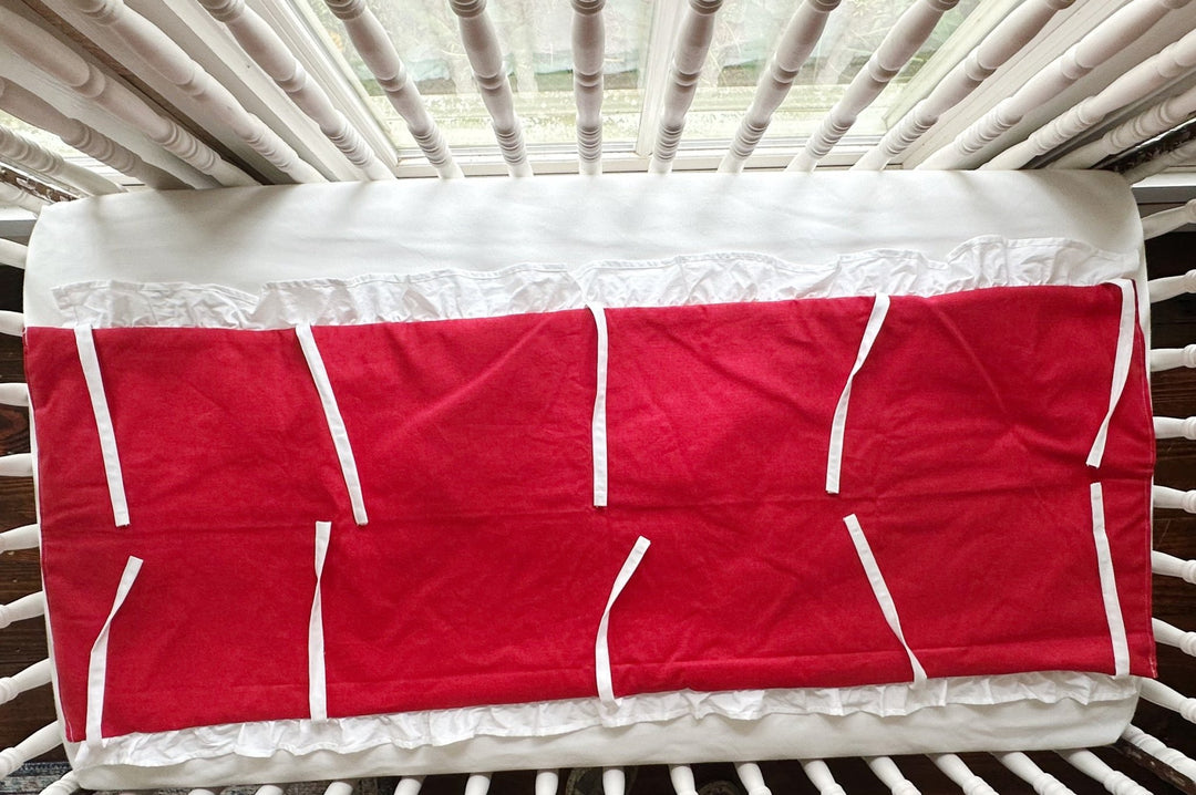 Cherry red ruffled crib rail cover laid flat, white ruffle along the edge and every white tie spread out