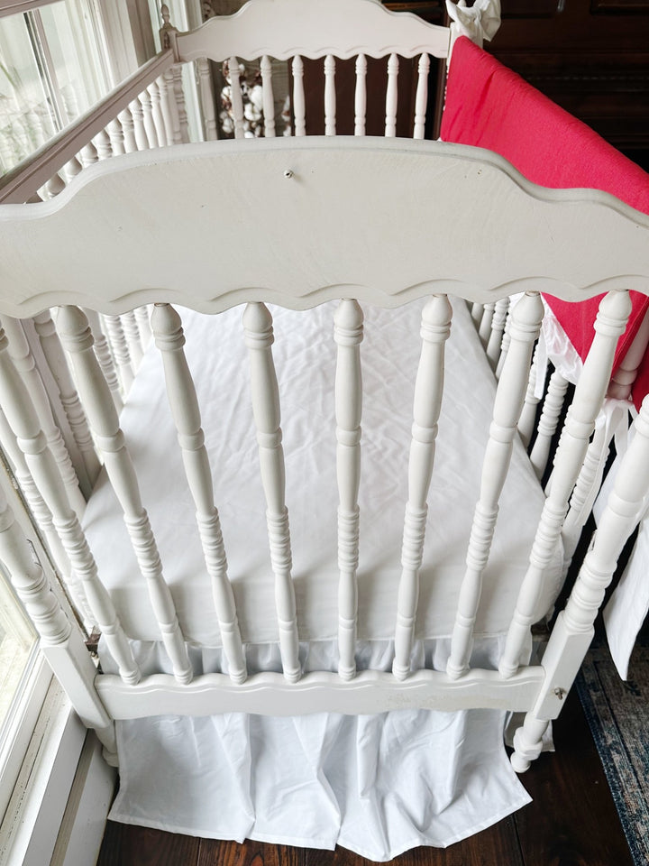 Looking down past the scalloped headboard at the white sheet and gathered white skirt