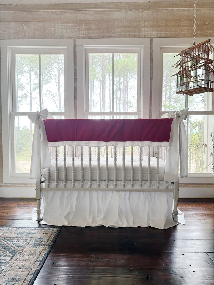 The red and white crib set in a pine-paneled nursery with three windows and a hanging birdcage