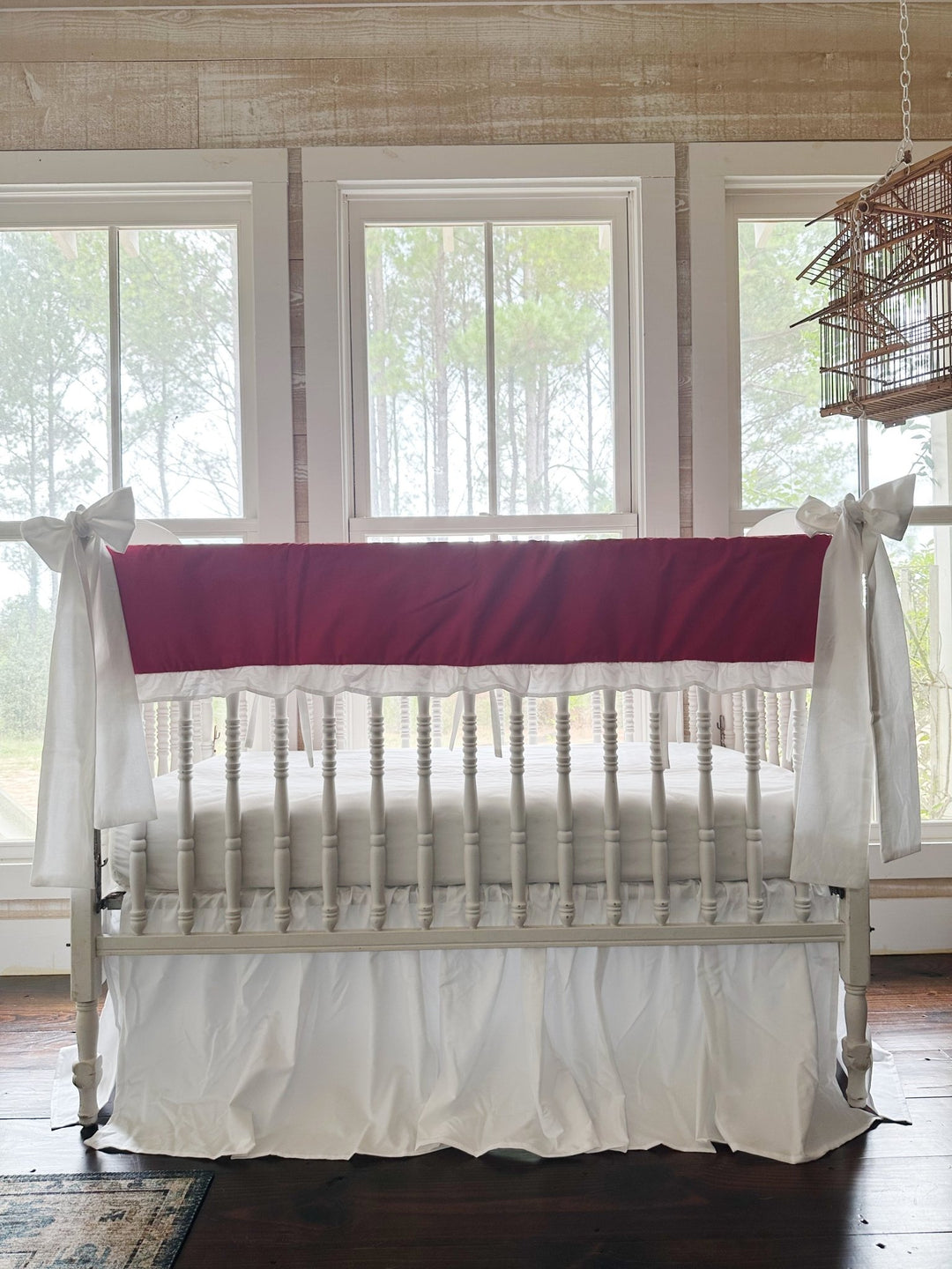 Bright red ruffled crib rail cover with a white ruffle, a white farmhouse skirt and two white bows on a spindle crib