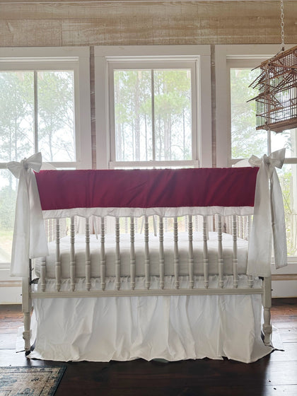 Bright red ruffled crib rail cover with a white ruffle, a white farmhouse skirt and two white bows on a spindle crib