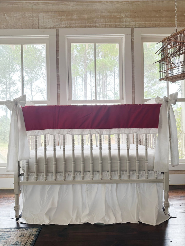 Bright red ruffled crib rail cover with a white ruffle, a white farmhouse skirt and two white bows on a spindle crib