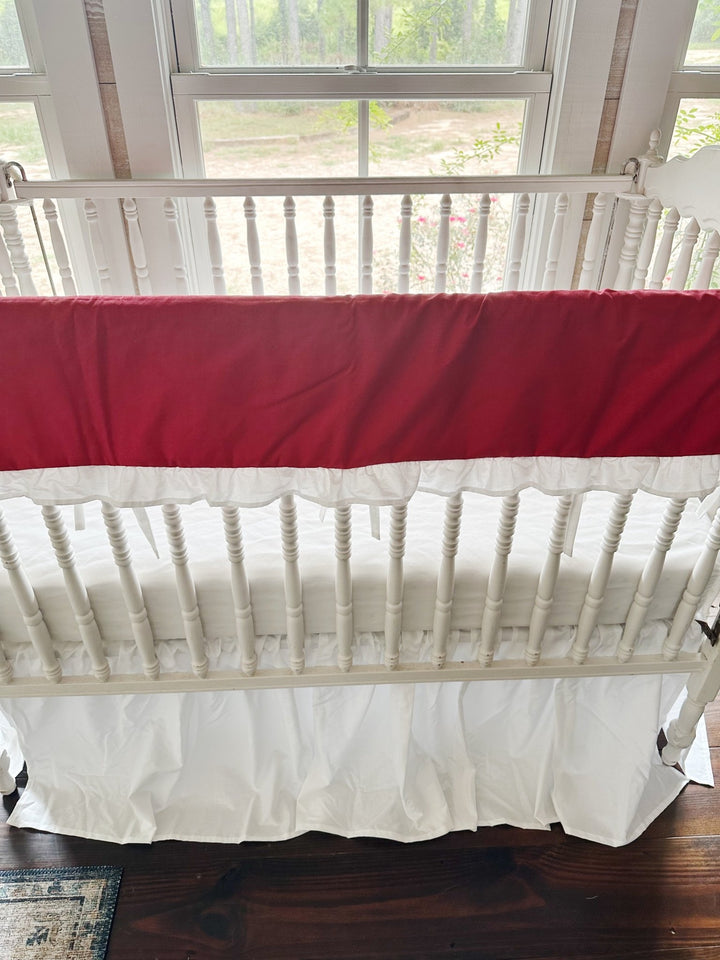 Straight-on view of the red rail cover with the white ties hanging between the crib spindles