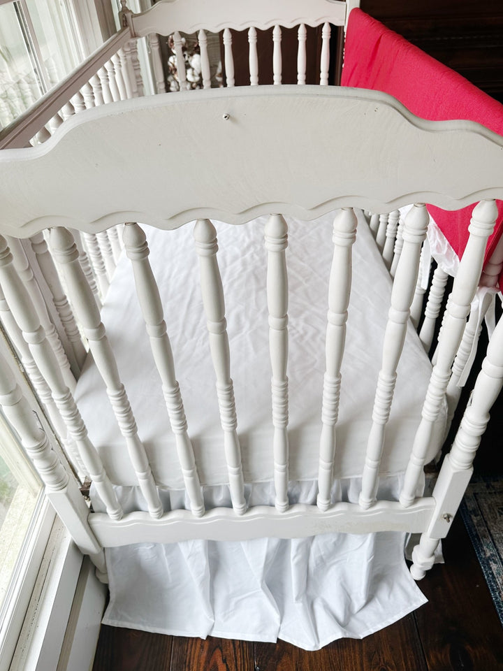 Looking down past the scalloped headboard at the white sheet and gathered white skirt