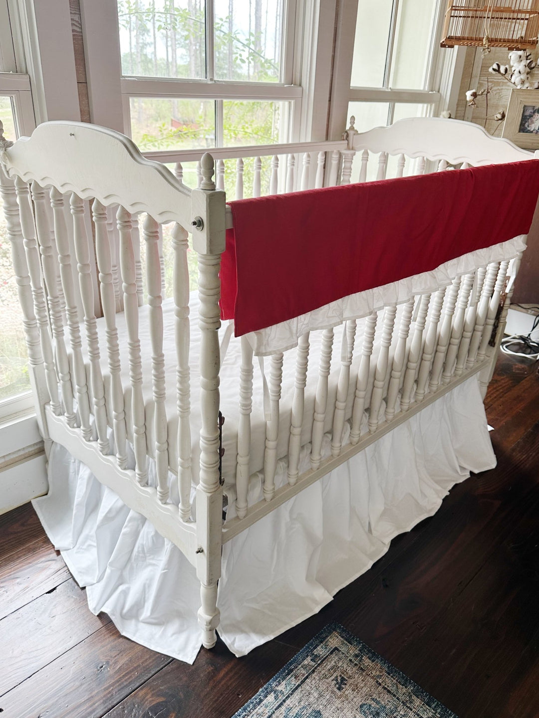 Corner view of the red rail cover running down the long rail of a white spindle crib