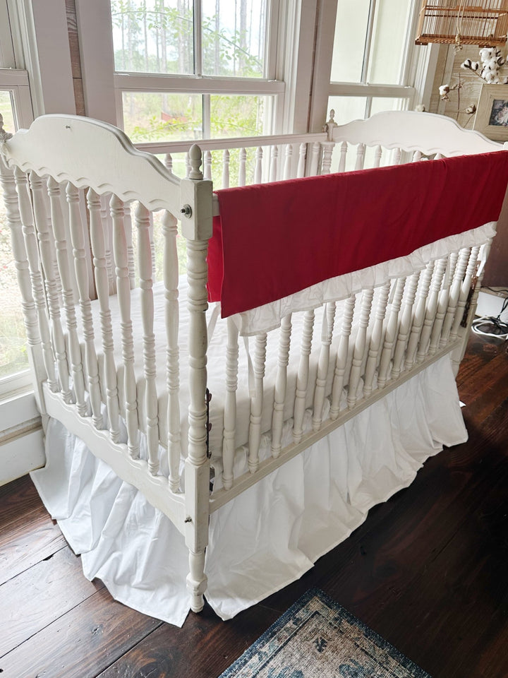 Corner view of the red rail cover running down the long rail of a white spindle crib