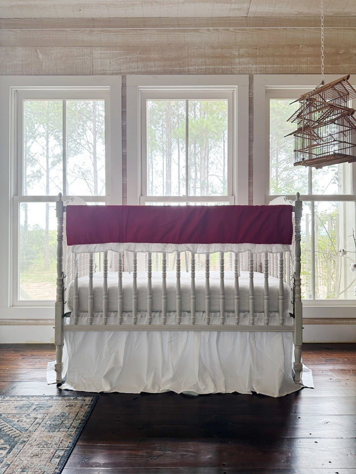 The two-piece red and white crib set in a pine-paneled nursery with windows and a hanging birdcage