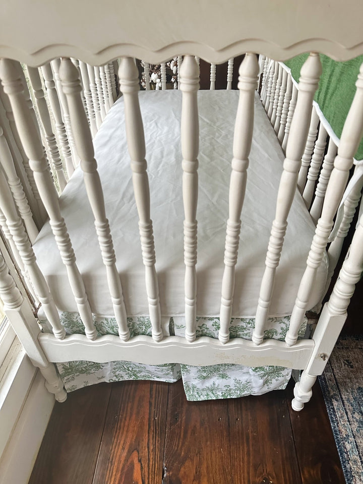 White fitted crib sheet inside the crib with the green toile box-pleat skirt below