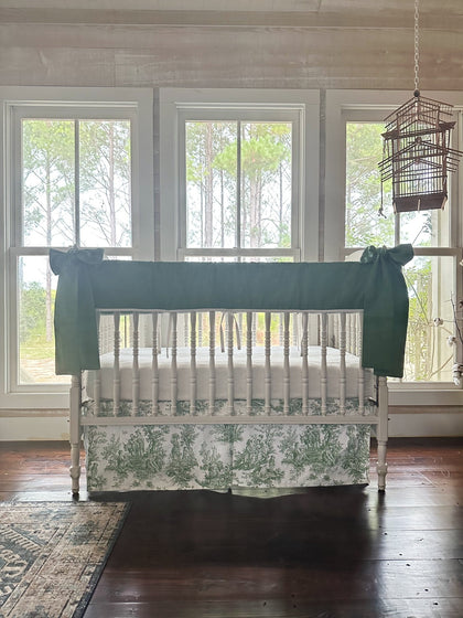 Green toile crib bedding set styled in a farmhouse nursery with pine trees through the windows
