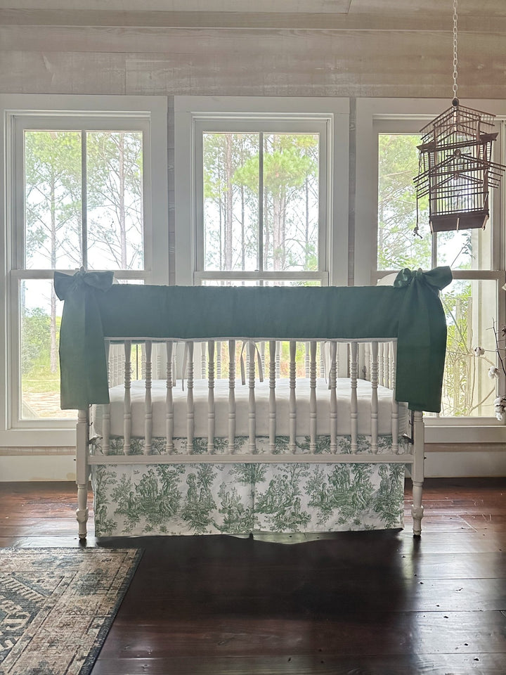 Green toile crib bedding set styled in a farmhouse nursery with pine trees through the windows