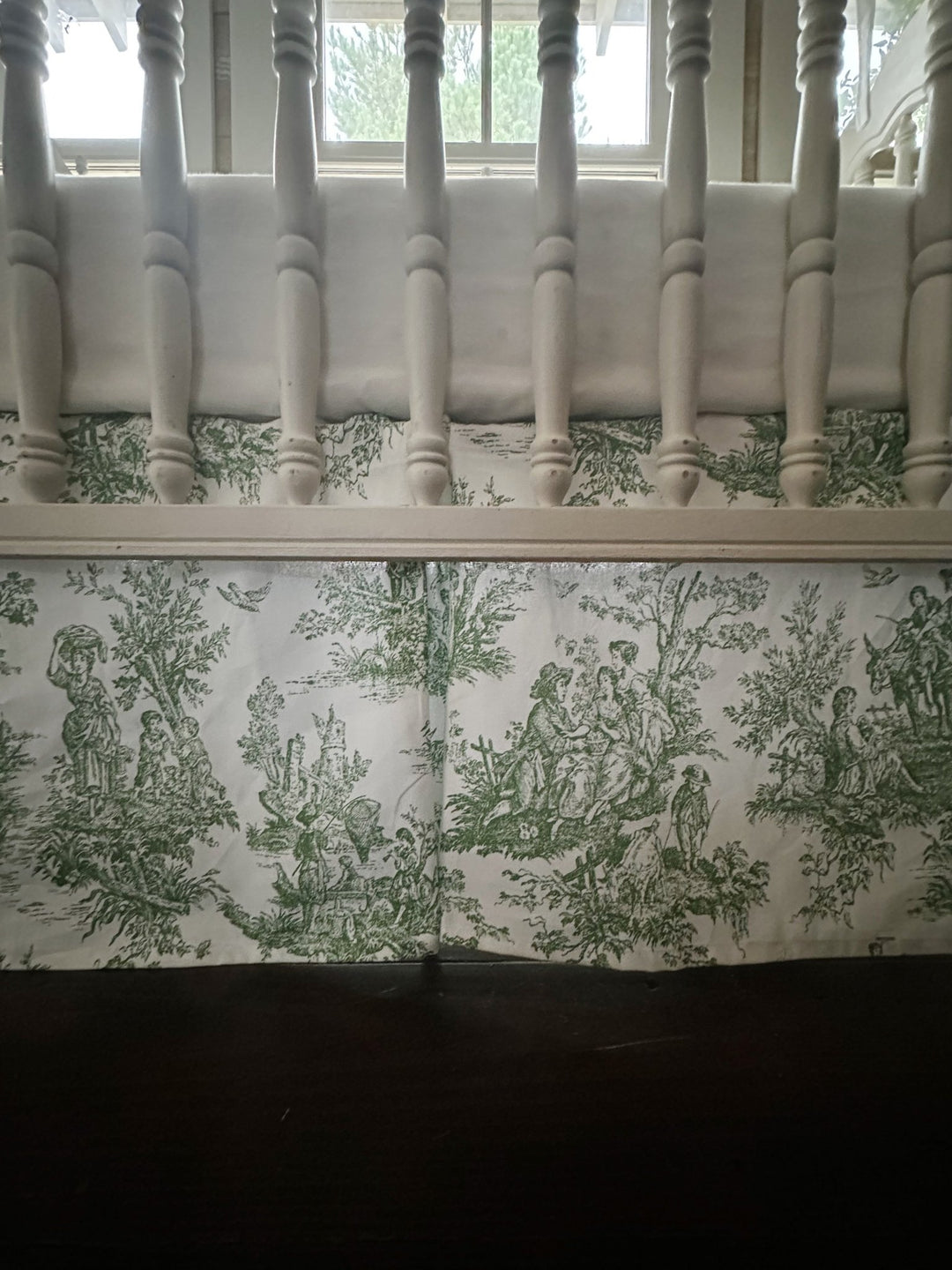 Pine green tailored crib rail cover with white cording and a green toile box-pleat crib skirt on a white spindle crib