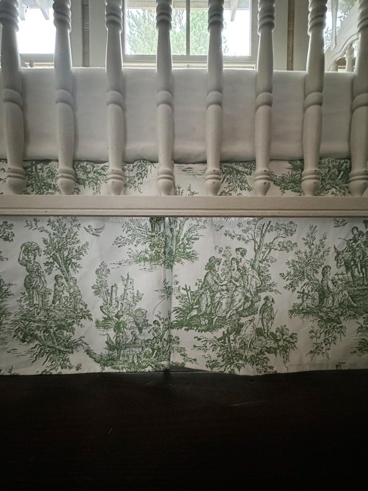 Pine green tailored crib rail cover with white cording and a green toile box-pleat crib skirt on a white spindle crib