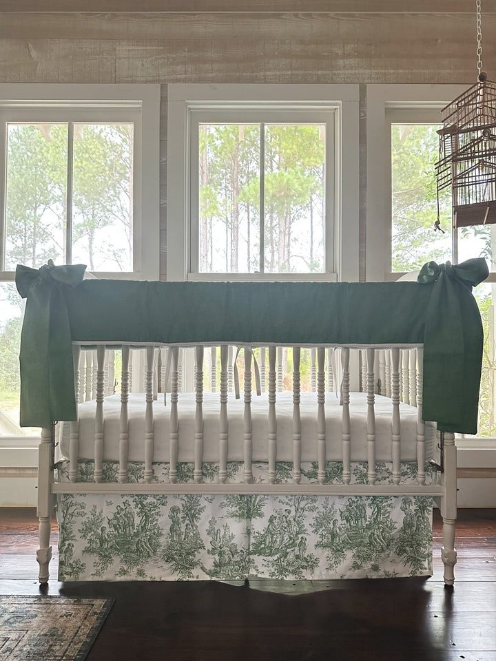 End view of the white spindle crib with the green toile tailored crib skirt and white sheet