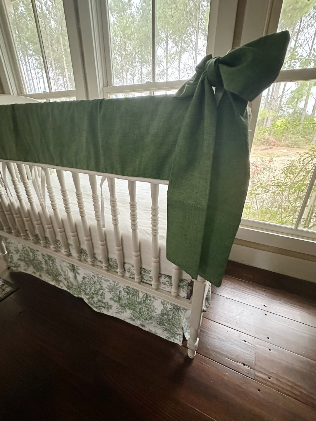 Close view of the pine green rail cover, white cording trim and a hand-tied green bow at the crib post