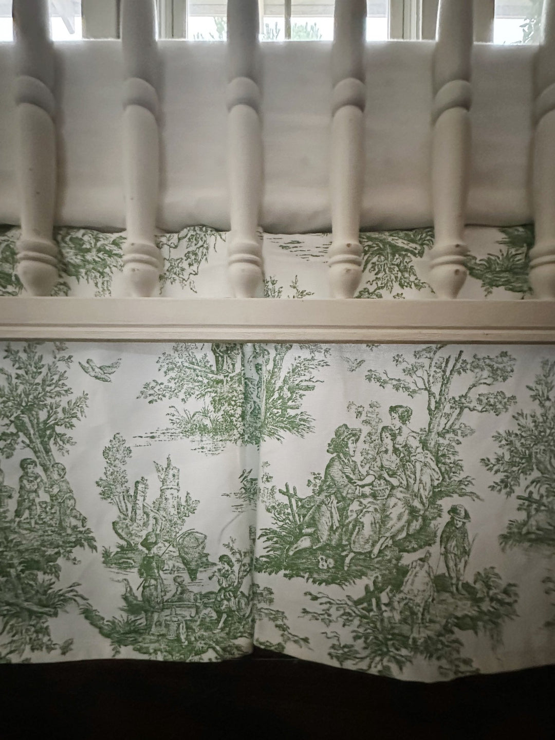 Green toile box-pleat crib skirt showing the scenic print and crisp corner pleat