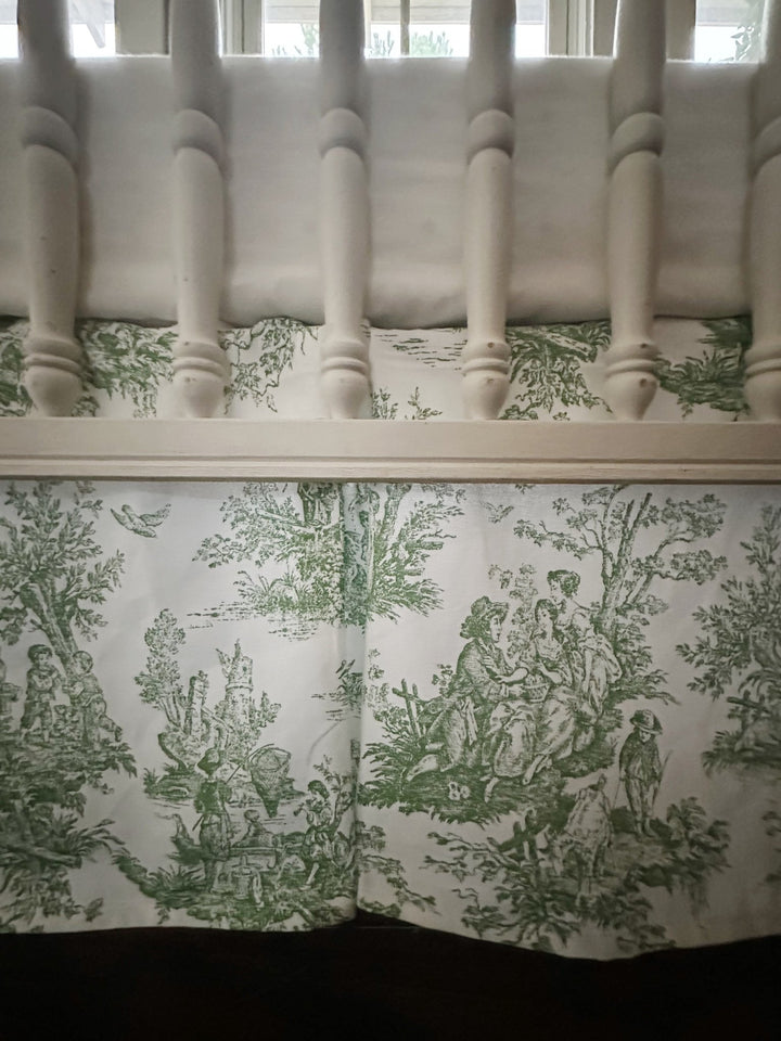 Green toile box-pleat crib skirt showing the scenic print and crisp corner pleat