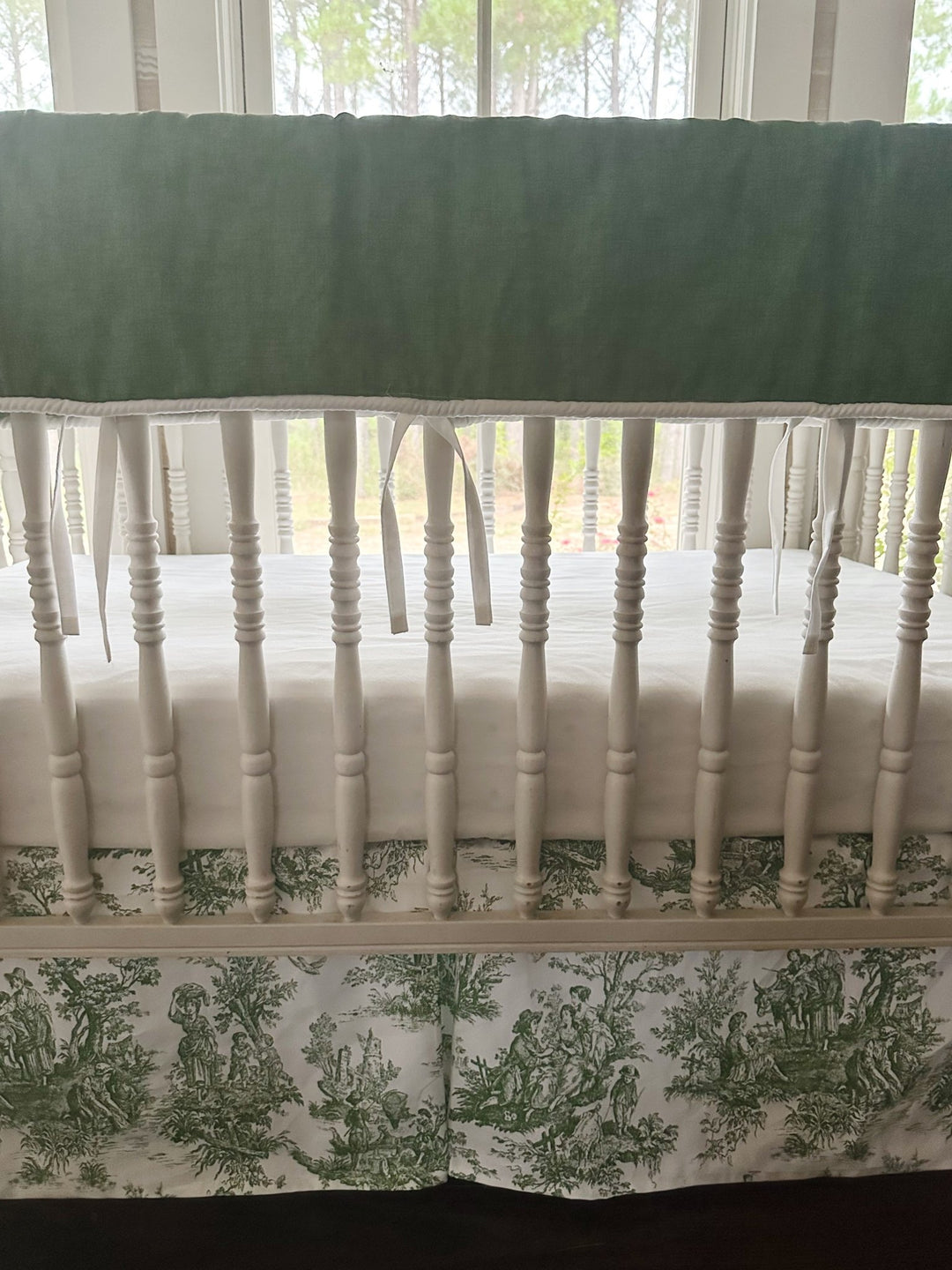 End view of the white spindle crib with the green toile box-pleat skirt and white crib sheet