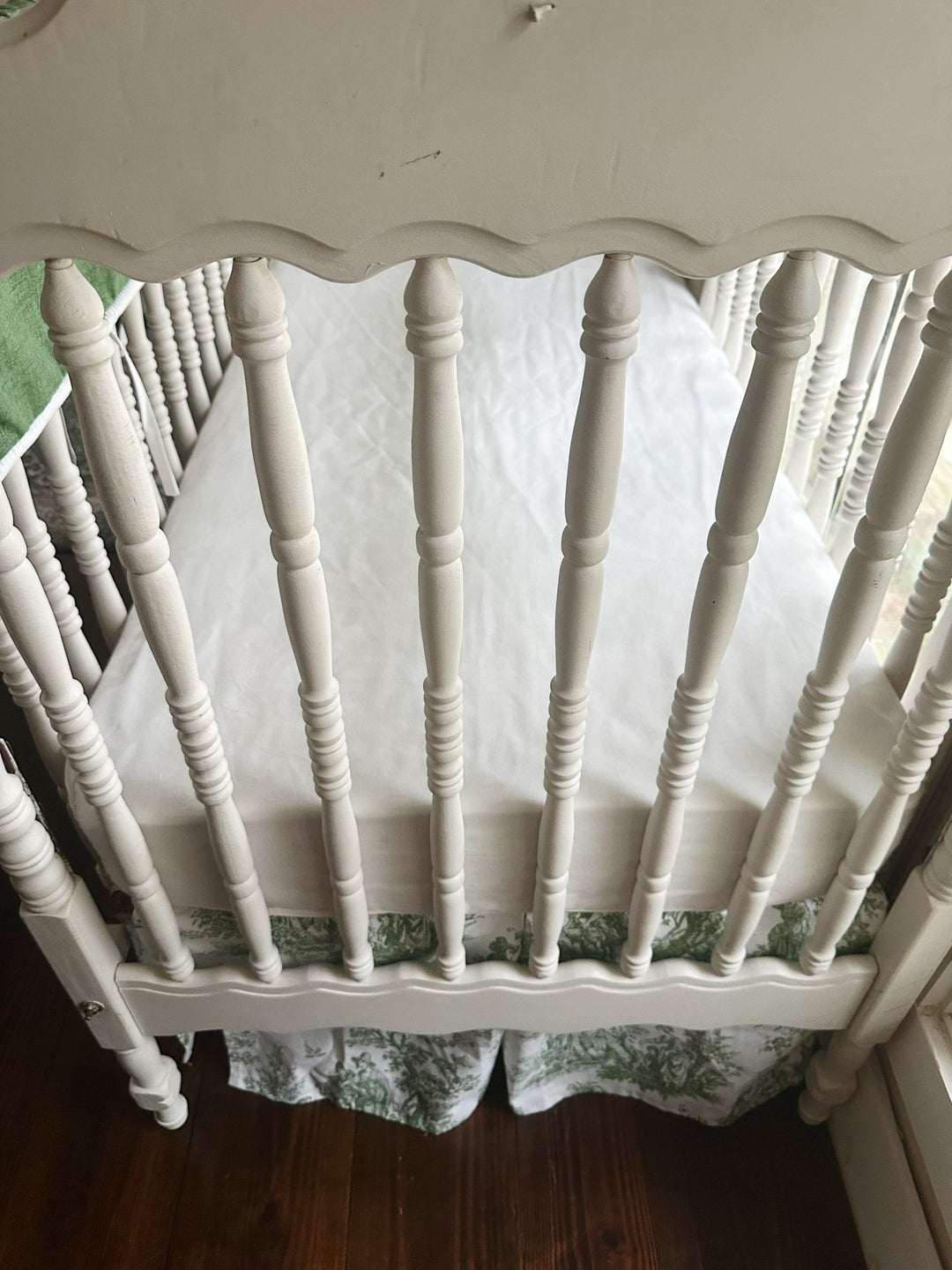 Cypress green tailored crib rail cover with white cording above a green toile box-pleat crib skirt