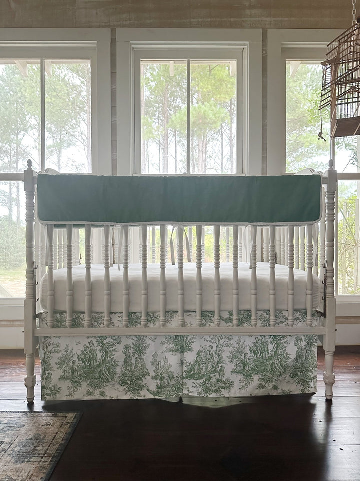 Green toile box-pleat crib skirt showing the scenic print and crisp corner pleat