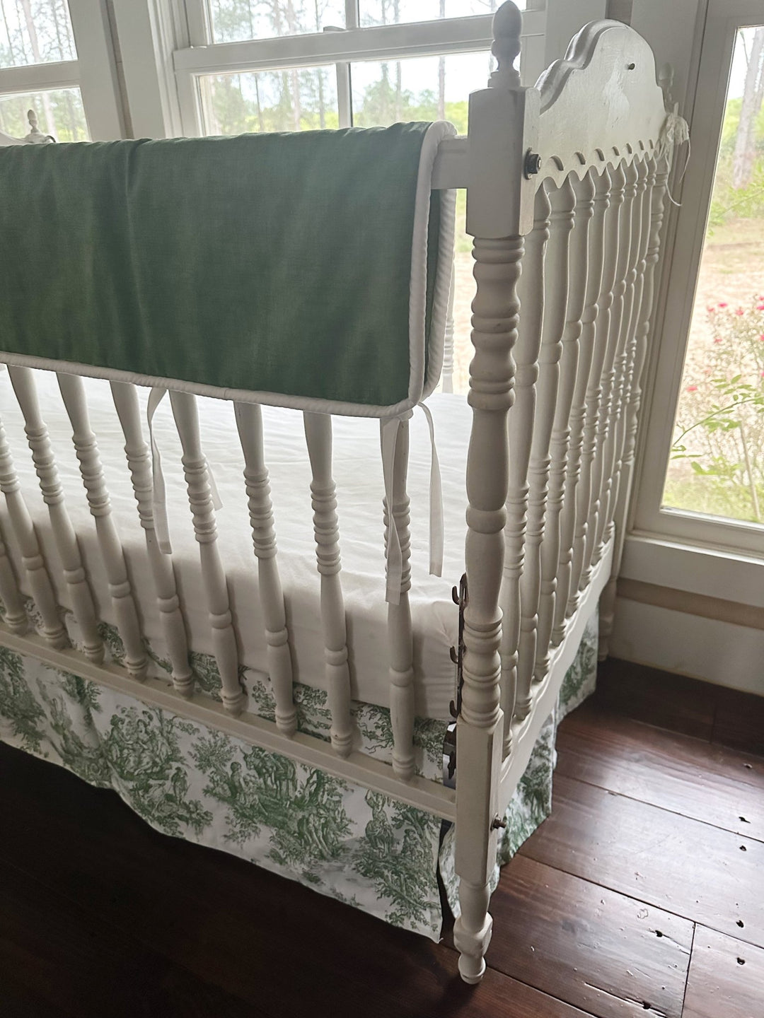 End of the cypress green tailored rail cover wrapping the crib rail beside the carved headboard