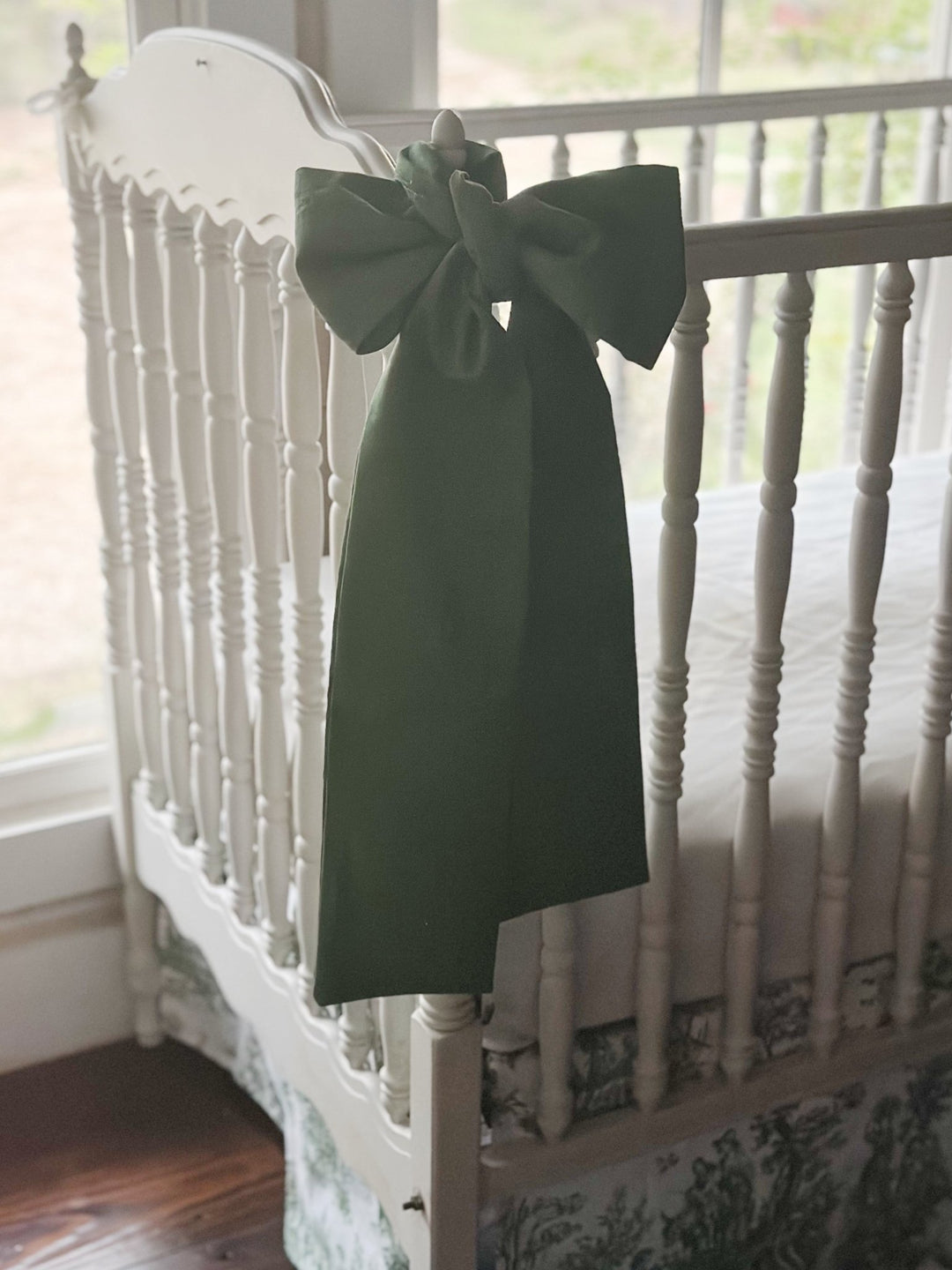 Cypress green bow on the corner post of a white spindle crib above a green toile skirt