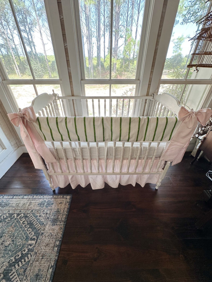 Overhead view of the whole crib showing the green stripe, white sheet and baby pink skirt