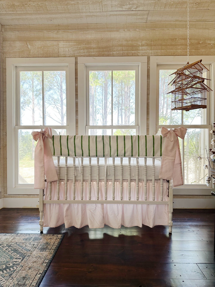 The pink and green Christmas crib set in a pine-paneled nursery with three tall windows and a hanging birdcage