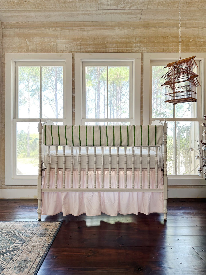 The pink and green crib set in a pine-paneled nursery with three tall windows and a hanging birdcage