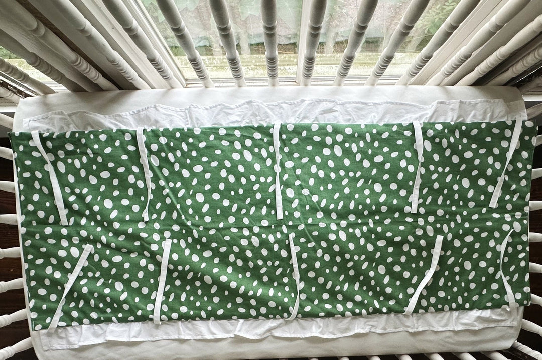 Green and white dot ruffled crib rail cover laid flat, white ruffle along the edge and every tie spread out