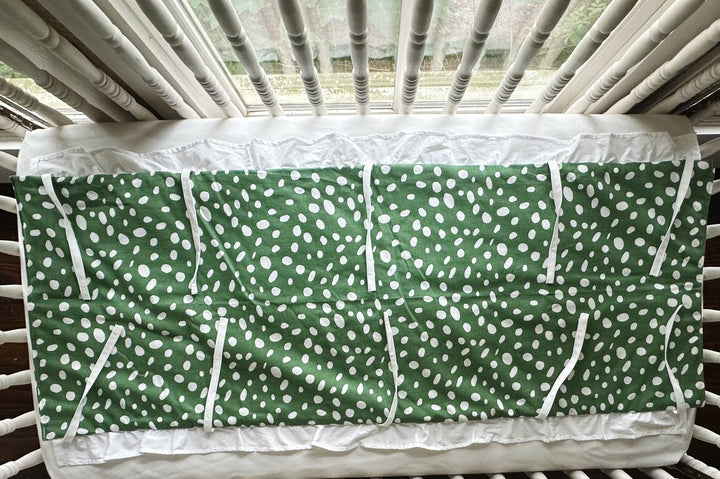 Green and white dot ruffled crib rail cover laid flat, white ruffle along the edge and every tie spread out