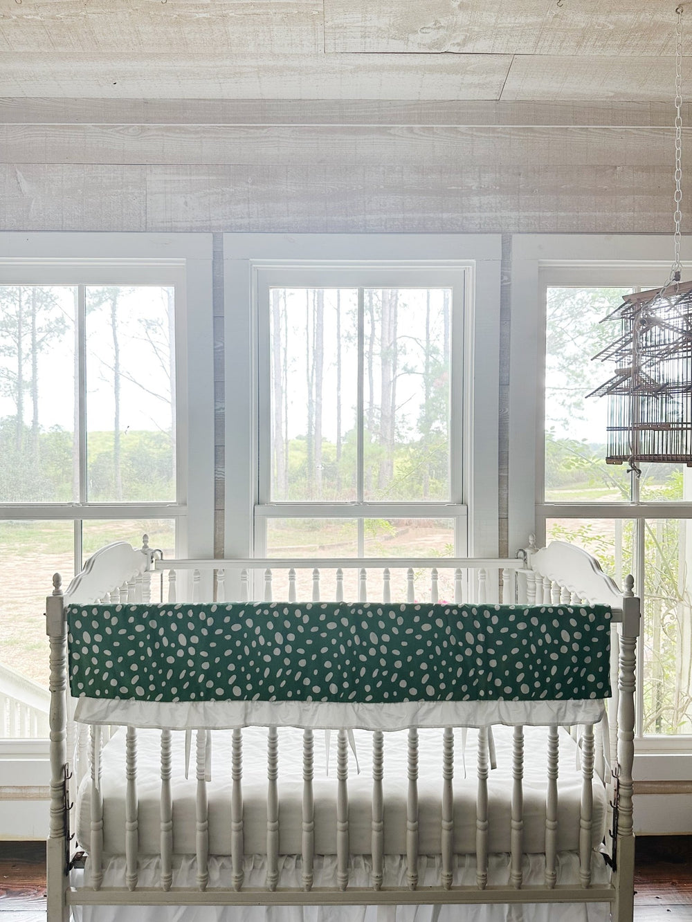 The green dot rail cover draped along the top rail of a white Jenny Lind style crib