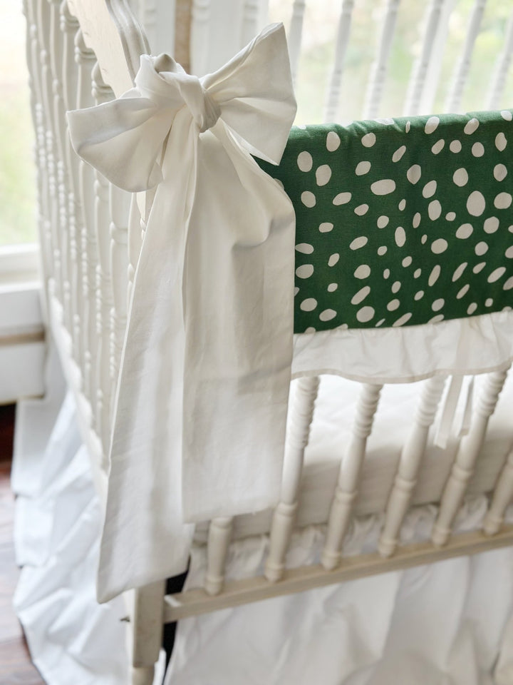 The white bow and the green dot rail cover seen together from the end of the crib