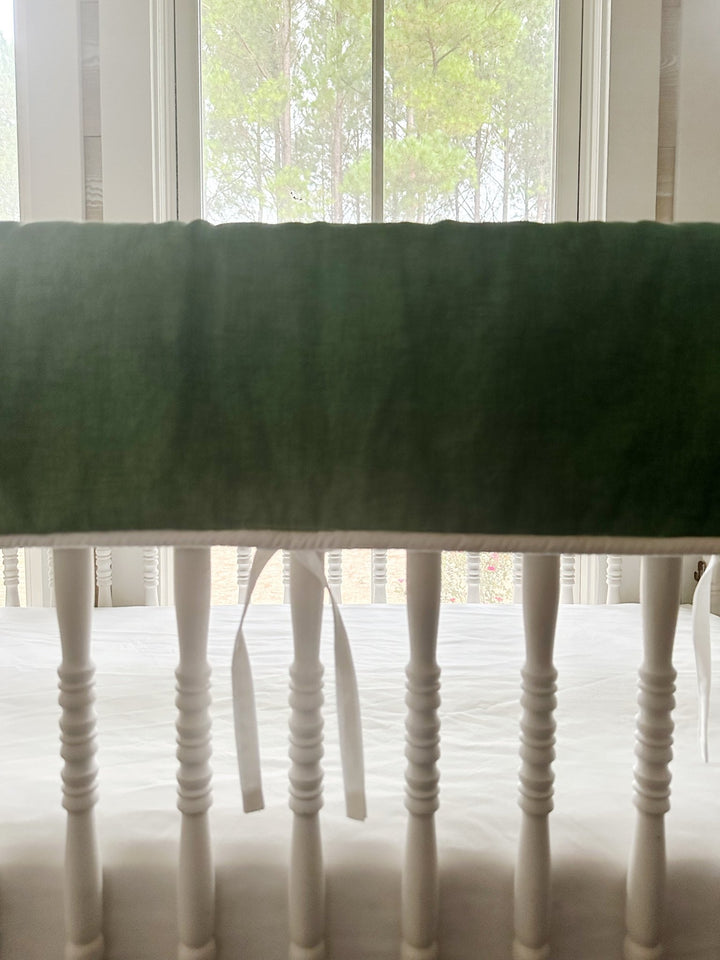 Straight-on view of the solid cypress green washed cotton panel with white ties hanging between crib spindles