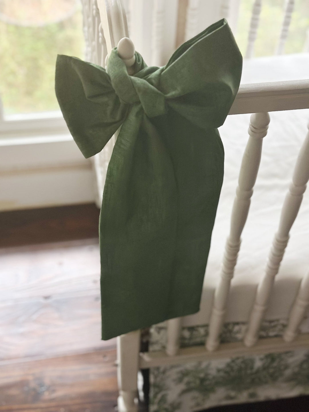 Cypress green bow seen from the side with its long sash tails hanging past the crib rail