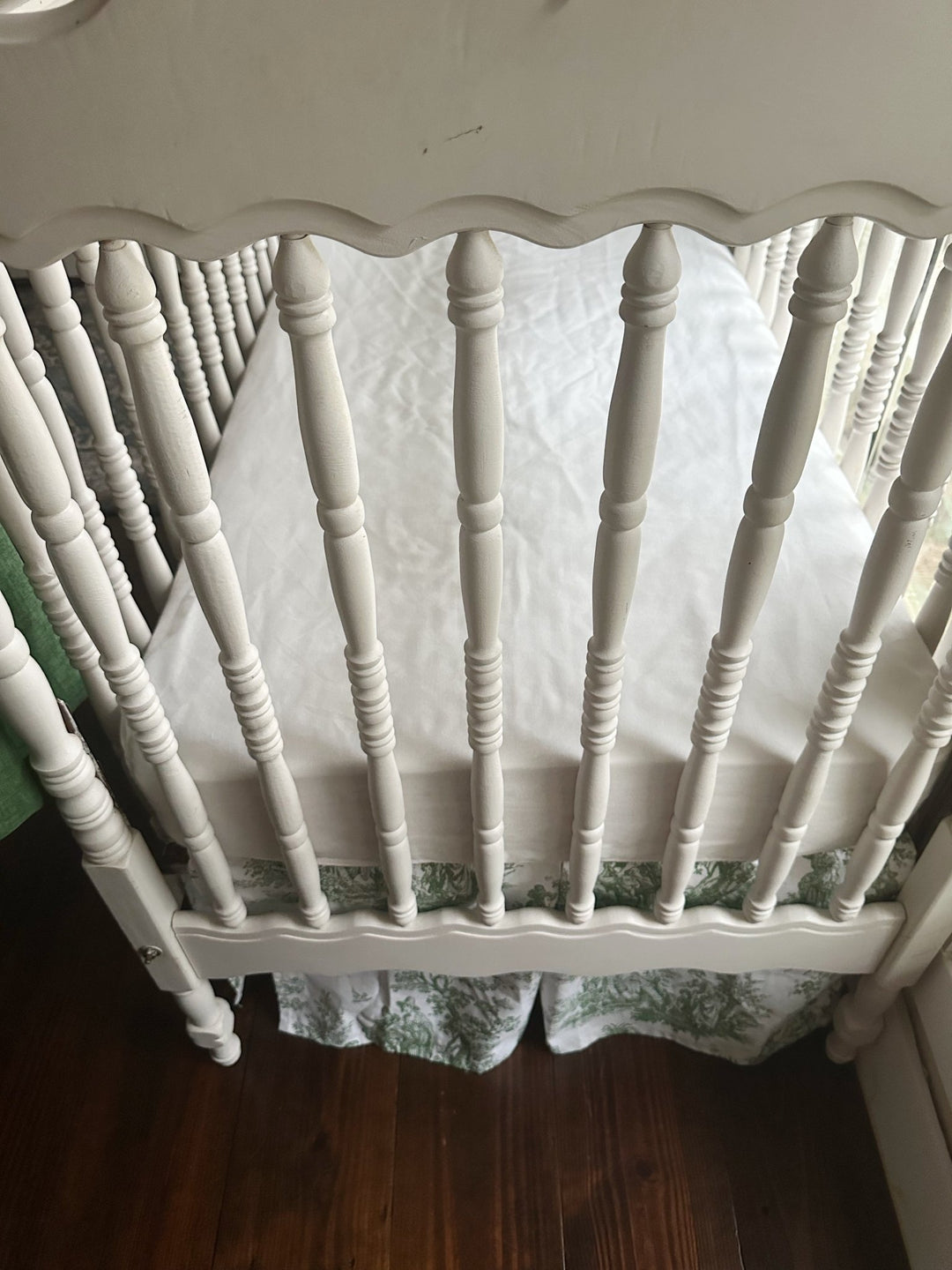 Foot of the crib showing the green toile skirt hanging evenly below the mattress platform