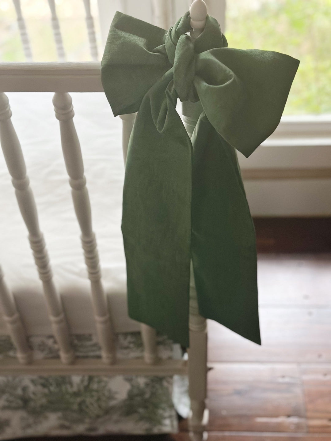 Large cypress green bow tied to a white crib post above the green toile skirt