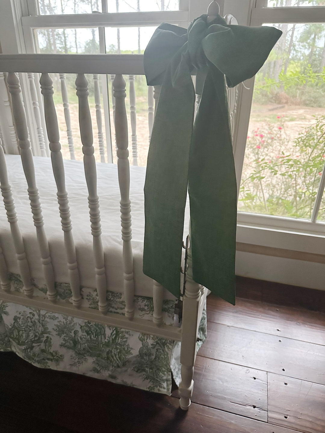 Cypress green bow on a crib post in afternoon light with the toile skirt below