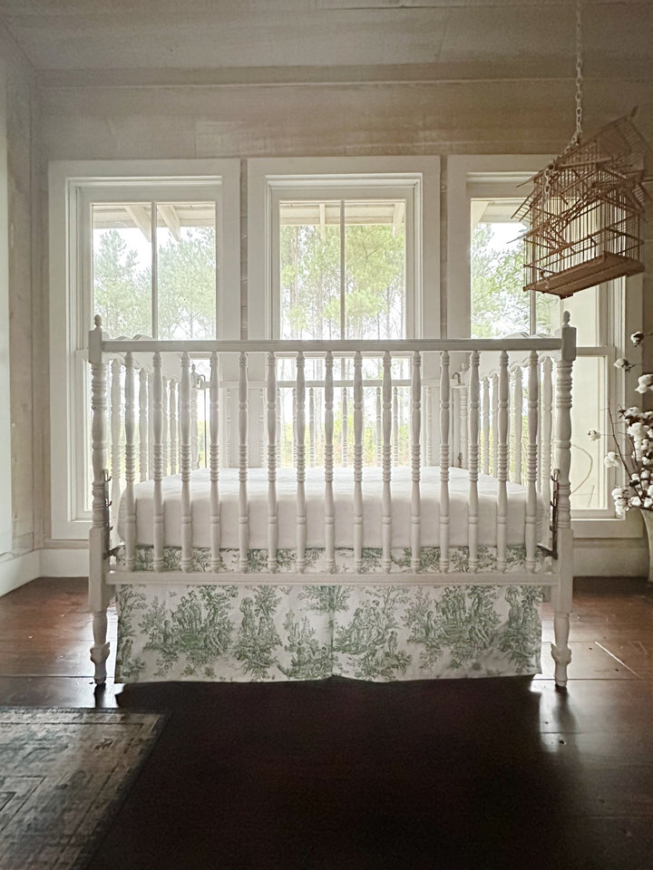 Green toile tailored crib skirt in a farmhouse nursery with pine woods through the windows