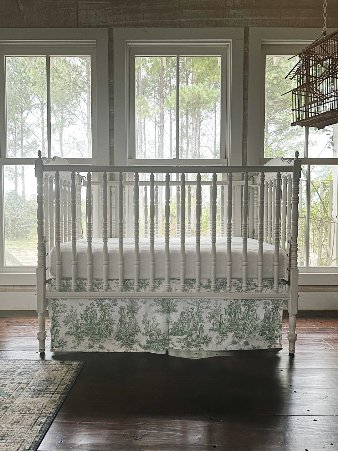 Green toile crib skirt across the front of the crib, pastoral figures visible along the panel