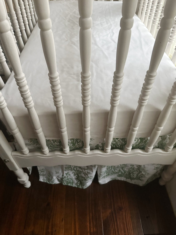 Looking down into the crib at the white sheet with the toile skirt deck below the mattress platform