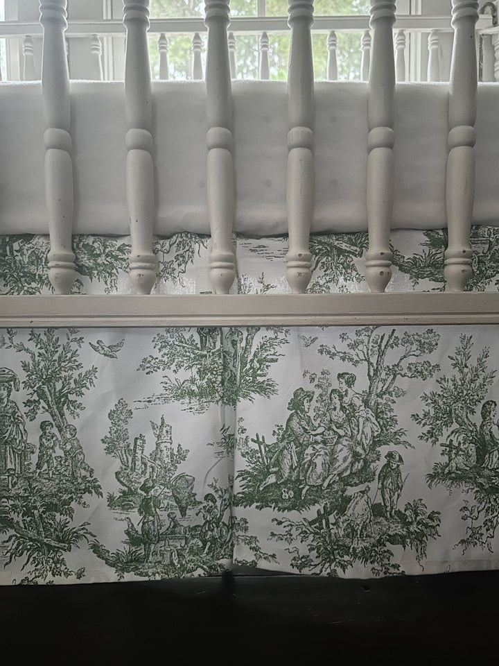 Split corner of the green toile crib skirt wrapping around a turned crib leg