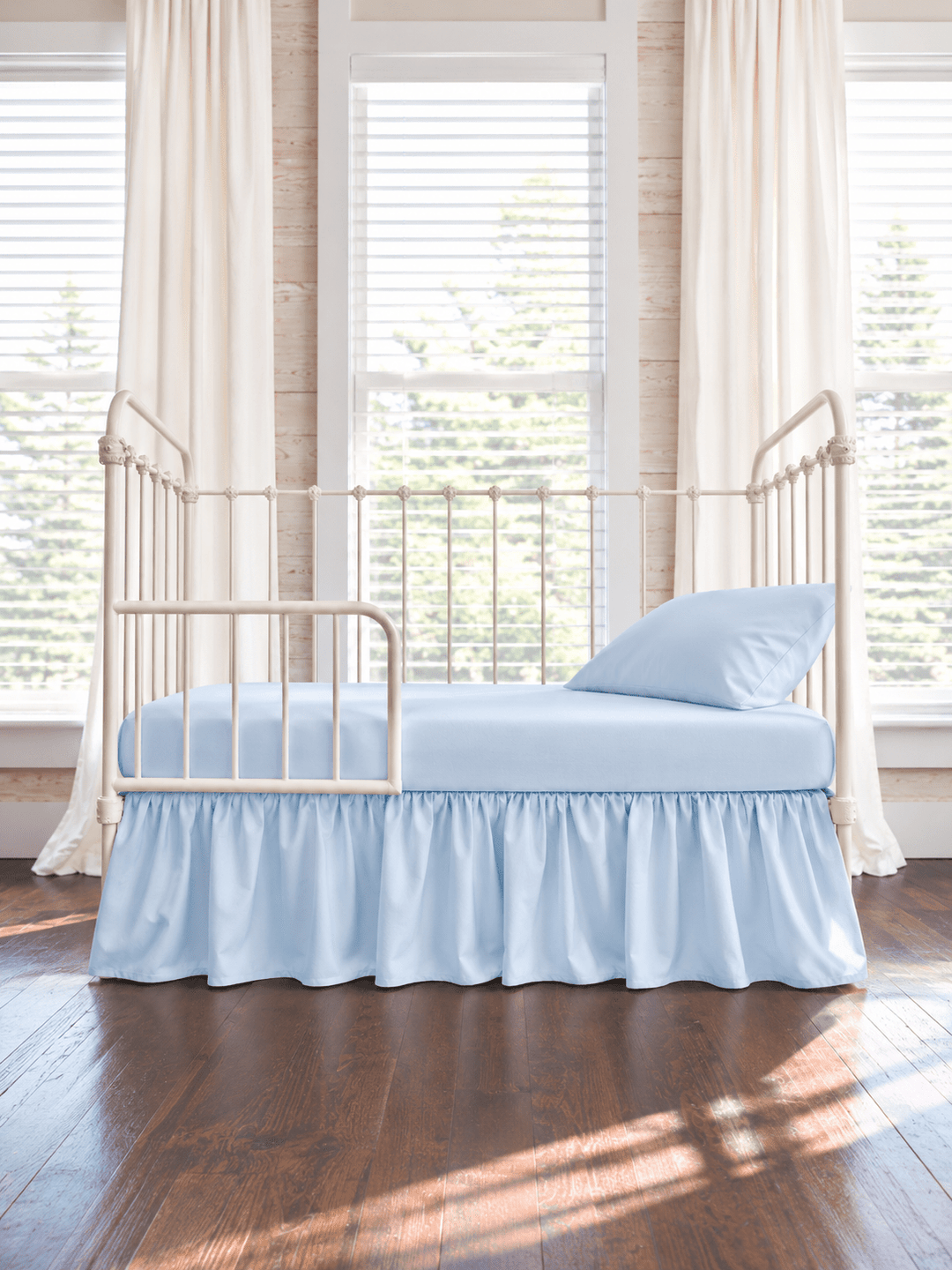 Heirloom Blue farmhouse toddler bed skirt gathered on all four sides of a cream iron crib converted to a toddler bed, with matching blue sheet and pillow - High Cotton Textile