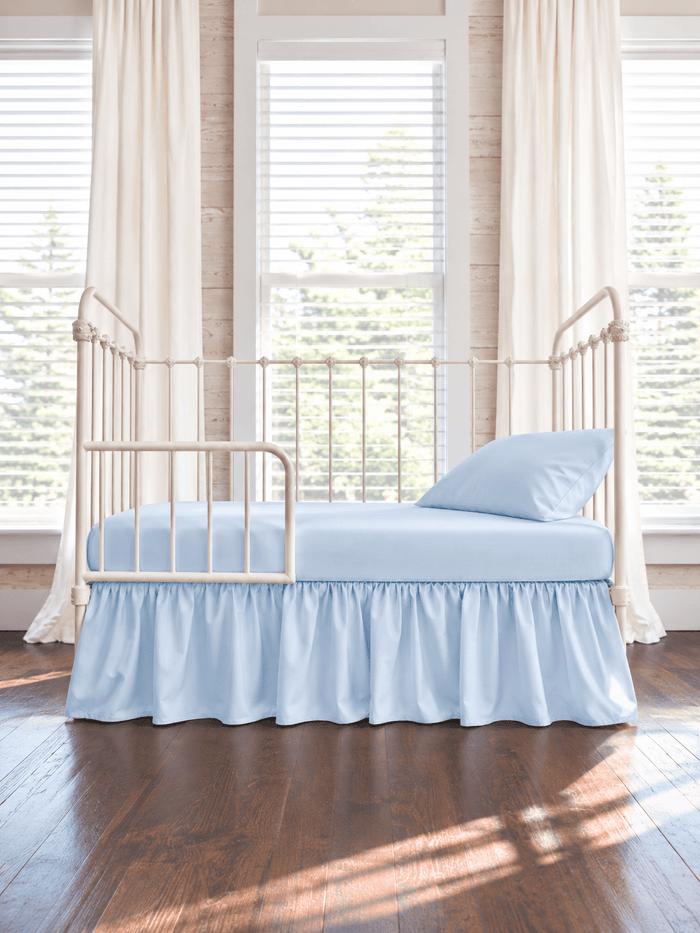 Heirloom Blue farmhouse toddler bed skirt gathered on all four sides of a cream iron crib converted to a toddler bed, with matching blue sheet and pillow - High Cotton Textile