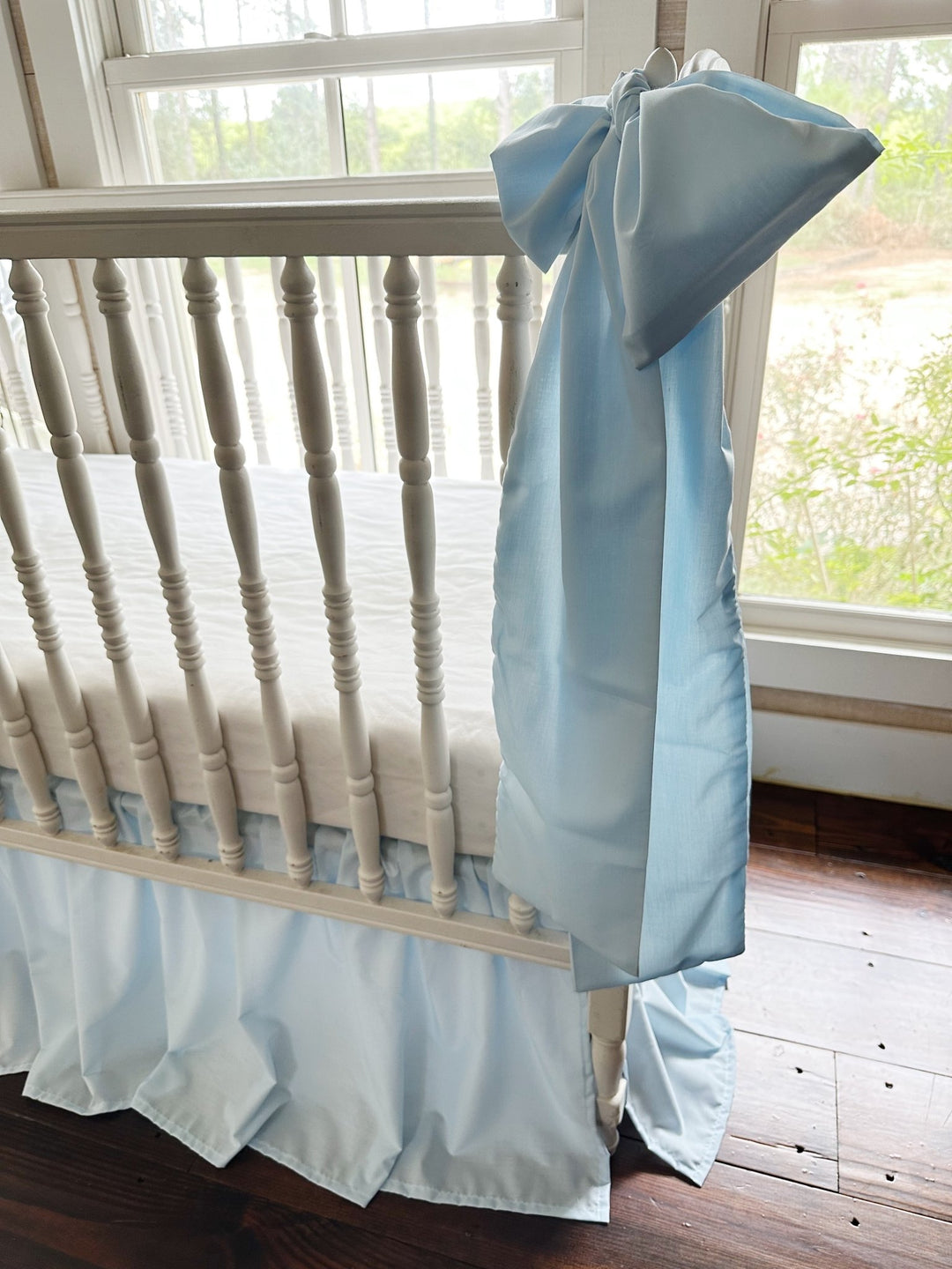 Large heirloom blue crib bow tied to the rail with long tails falling past the skirt