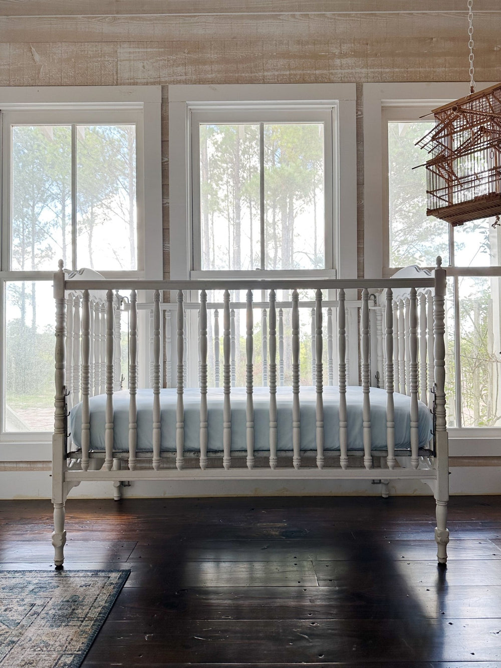 White spindle crib made up with a Heirloom Blue fitted crib sheet, in a nursery with pine windows and dark wood floors - High Cotton Textile